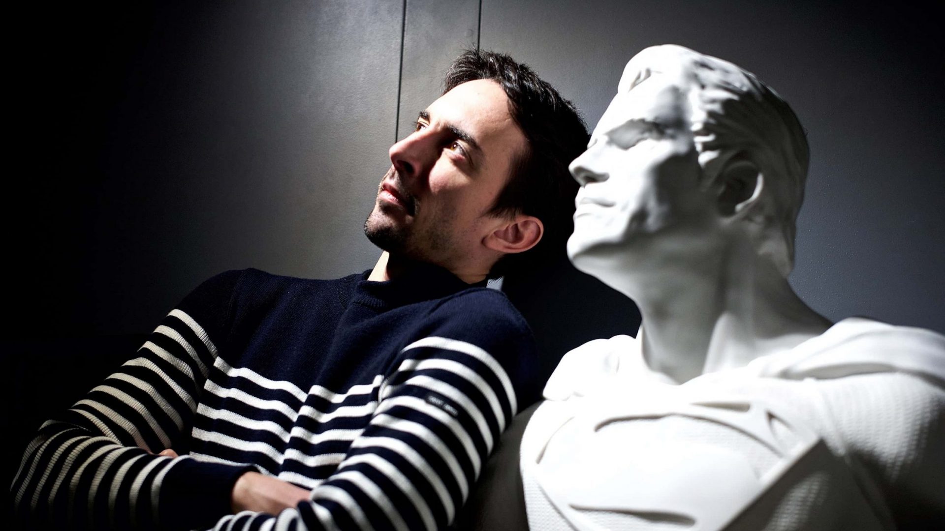 Picture of French artist Leo Caillard, next to a marble sculpture of Superman